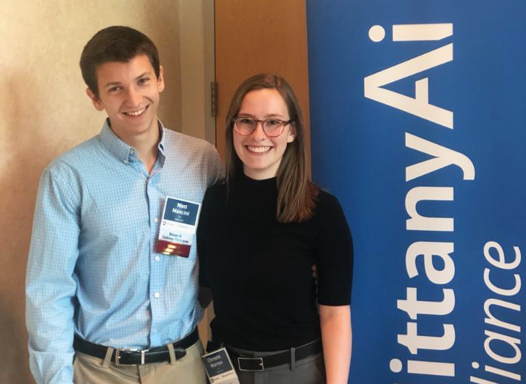 Matthew Mancini, left, and Christie Warren pose next to the Nittany AI Challenge banner.