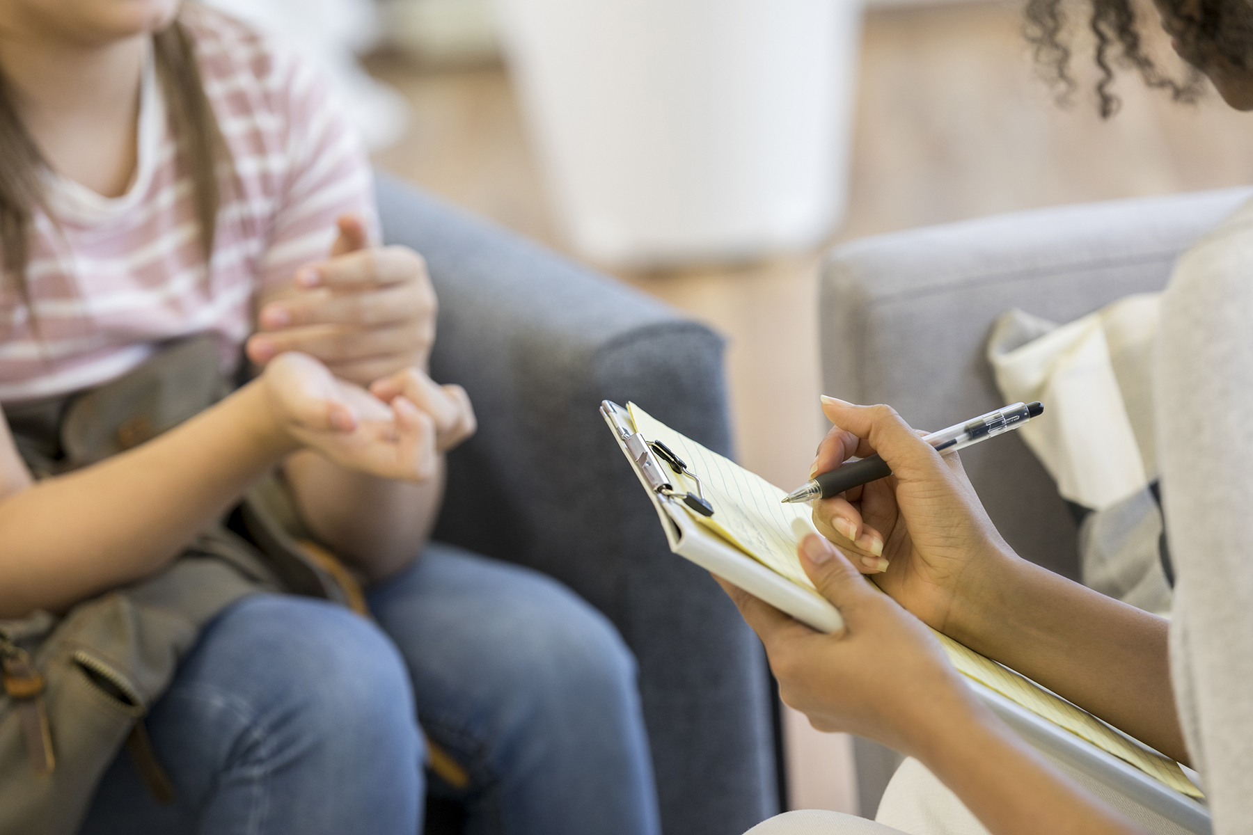 Unrecognizable teenage girl shares her troubles with a female mental health professional. The mental health professional is taking notes.