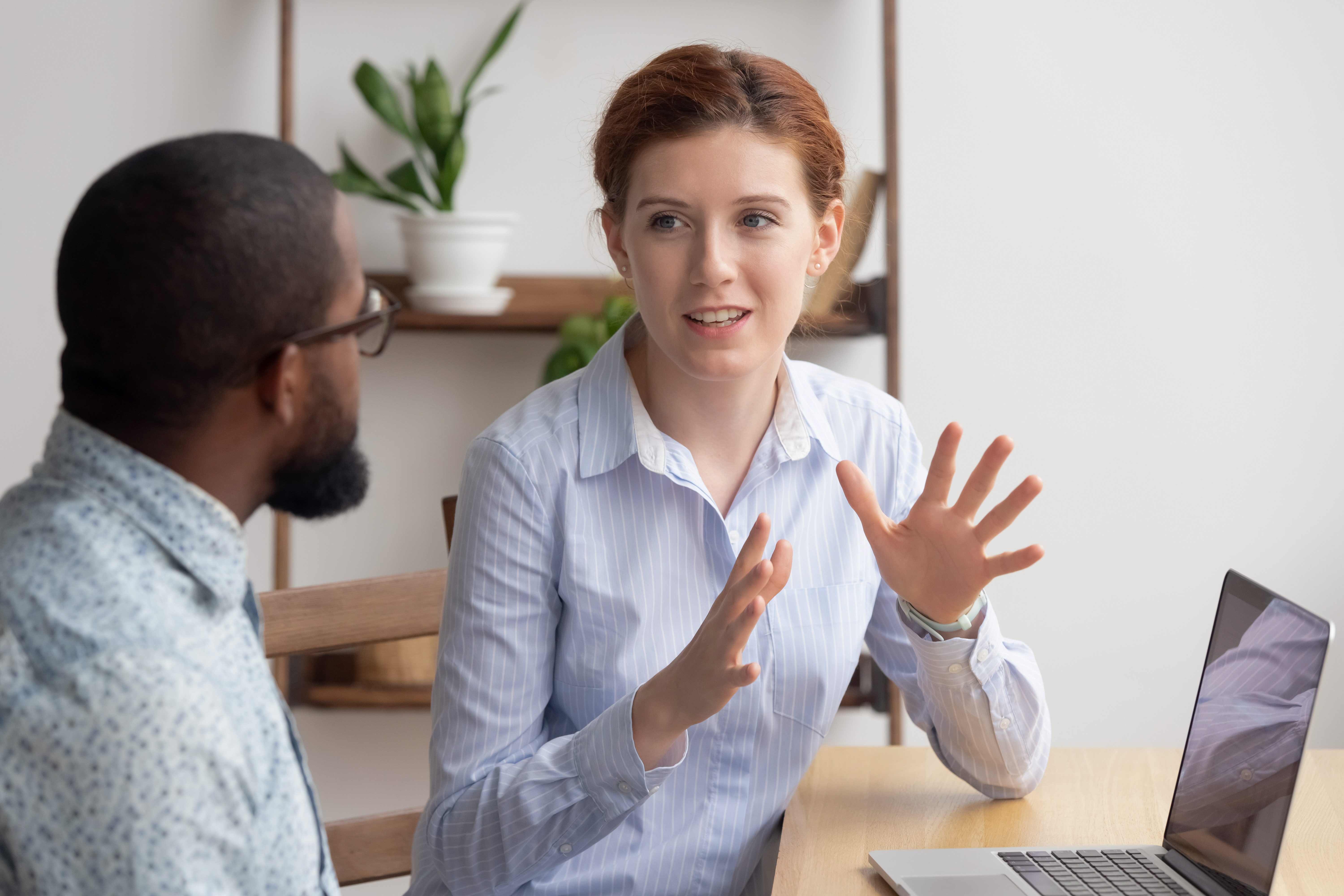 Man and woman talking near a laptop computer in an office setting. 