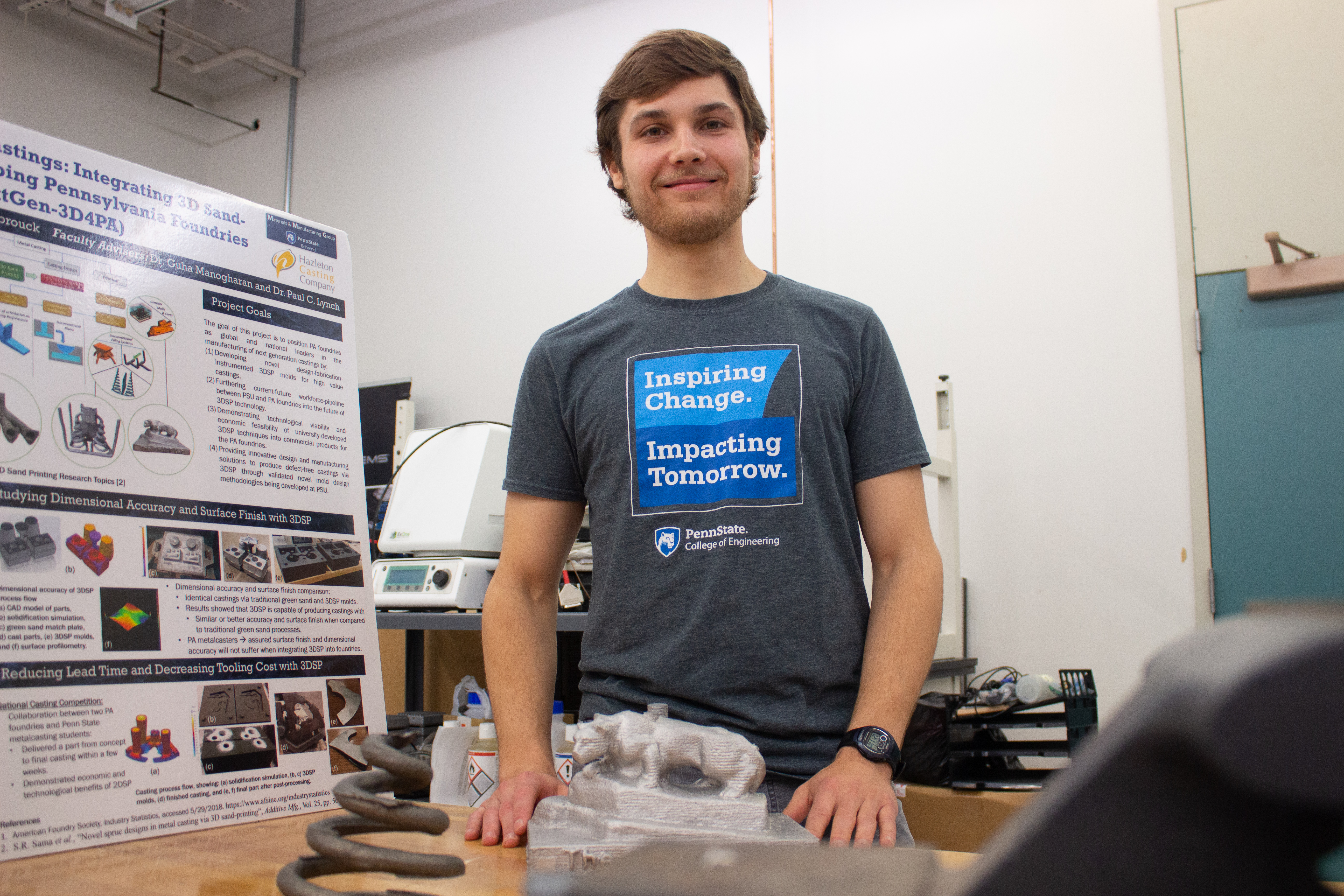 A man stands in an additive manufacturing lab with posters and equipment.