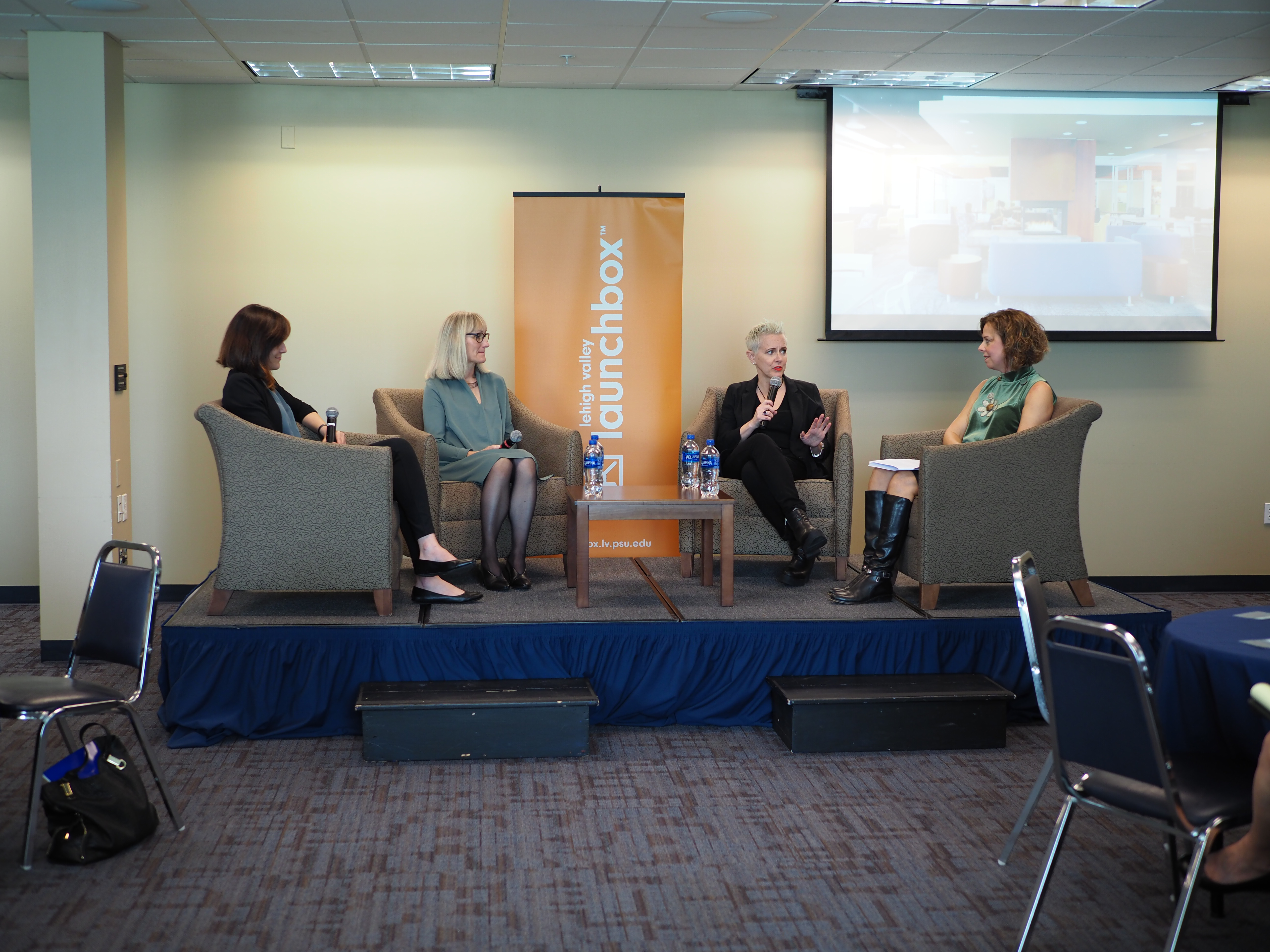 Four women on raised stage speaking at a luncheon