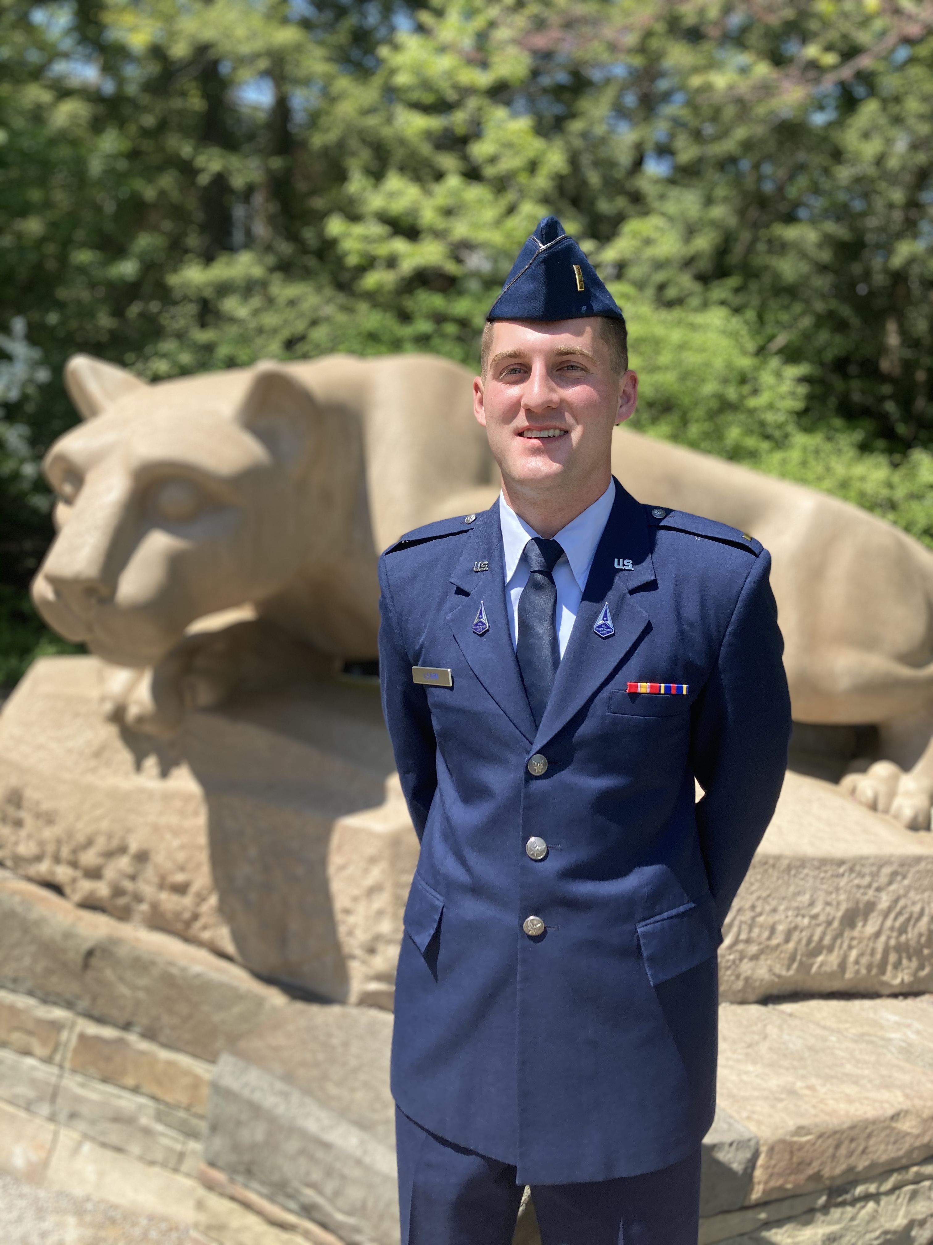 person dressed in air force uniform stands at ease in front of lion status for picture.