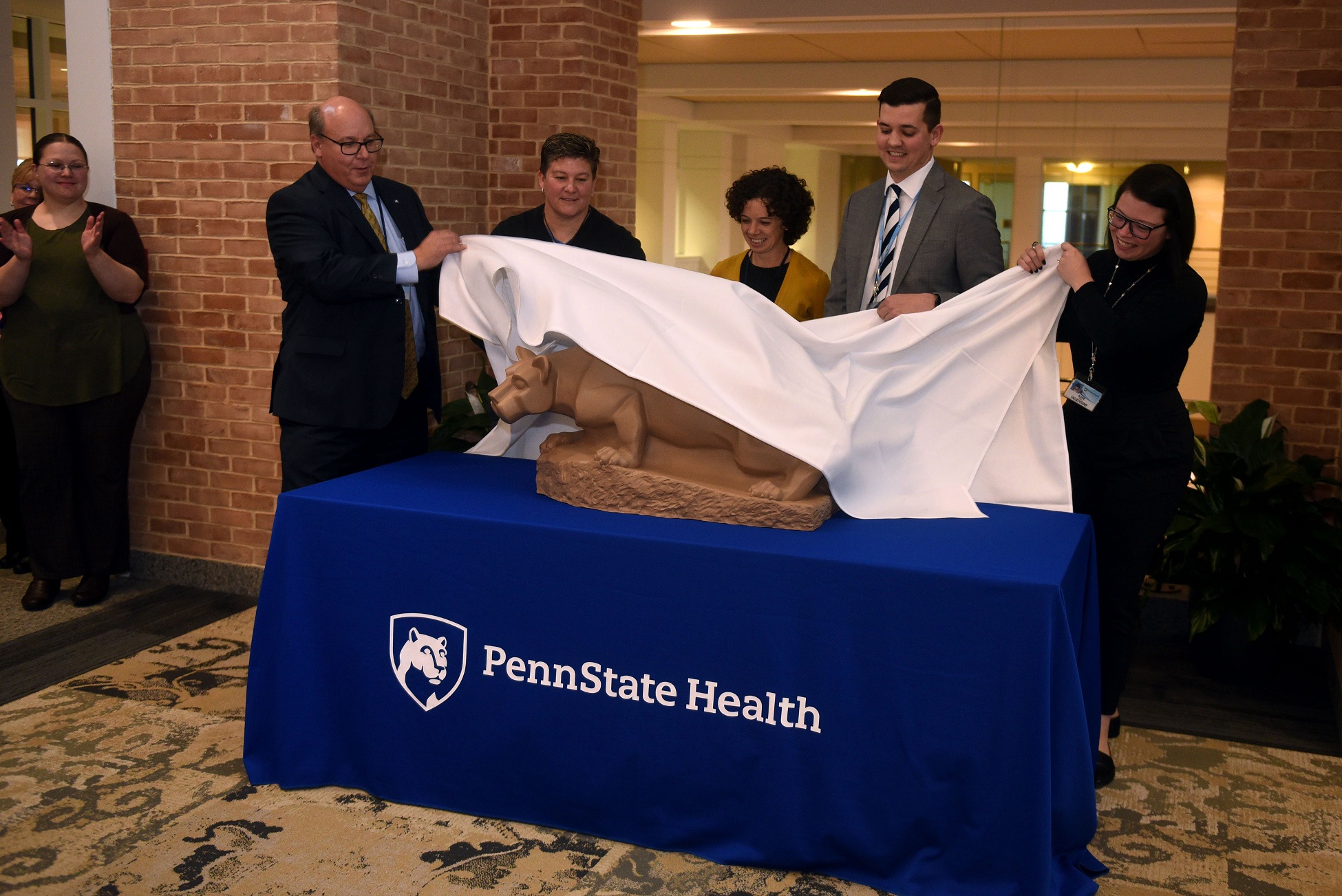 Five people take a cloth off to reveal a statue of a lion