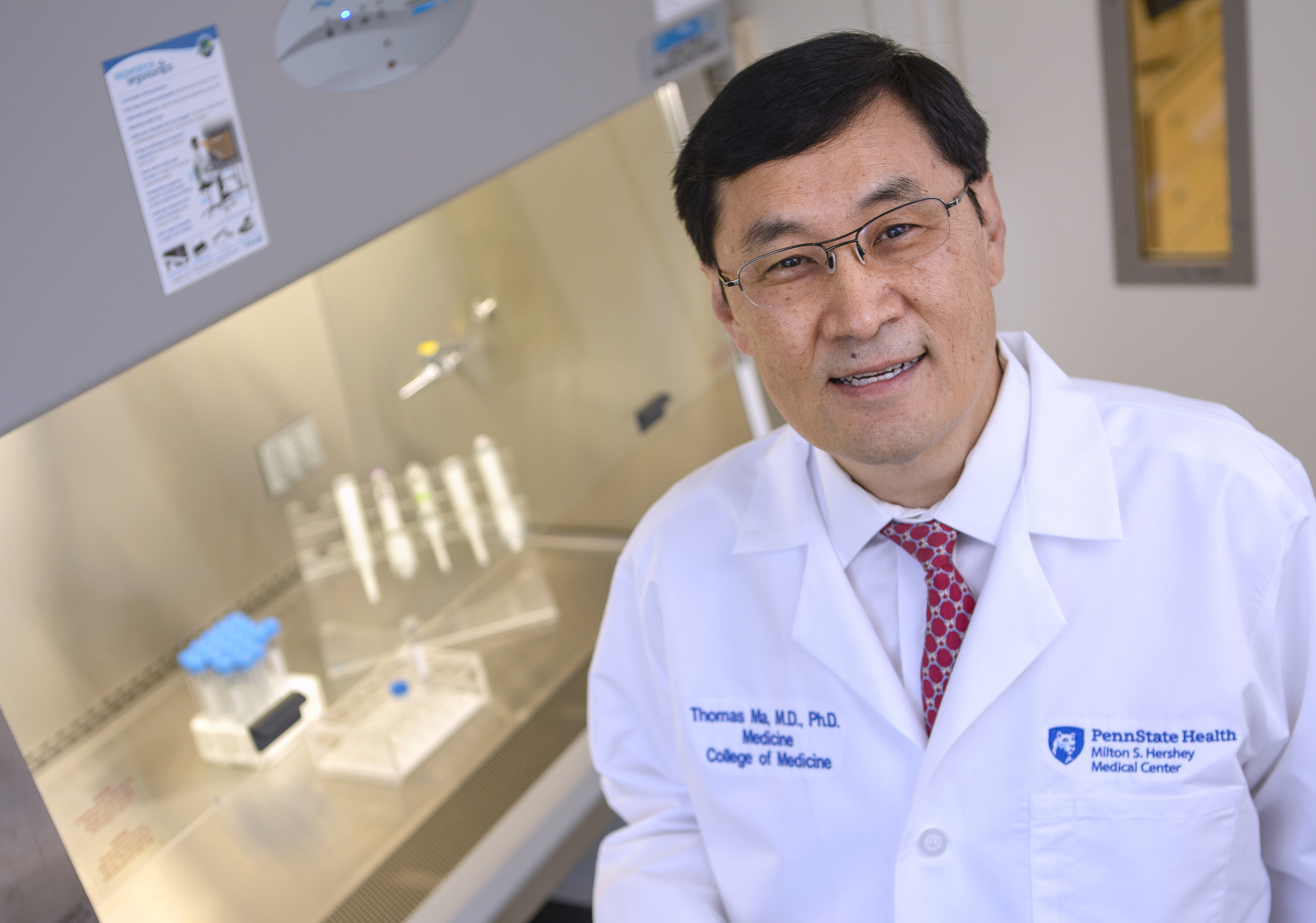 Dr. Thomas Ma poses for a photo, with a lab workbench and equipment in the background.