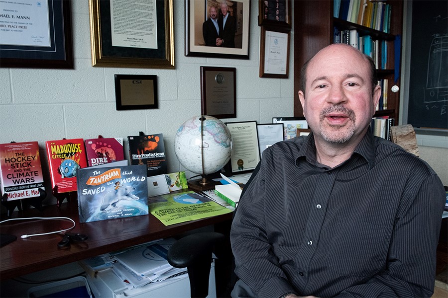 Michael Mann sitting in front of a table holding his many books on climate science.