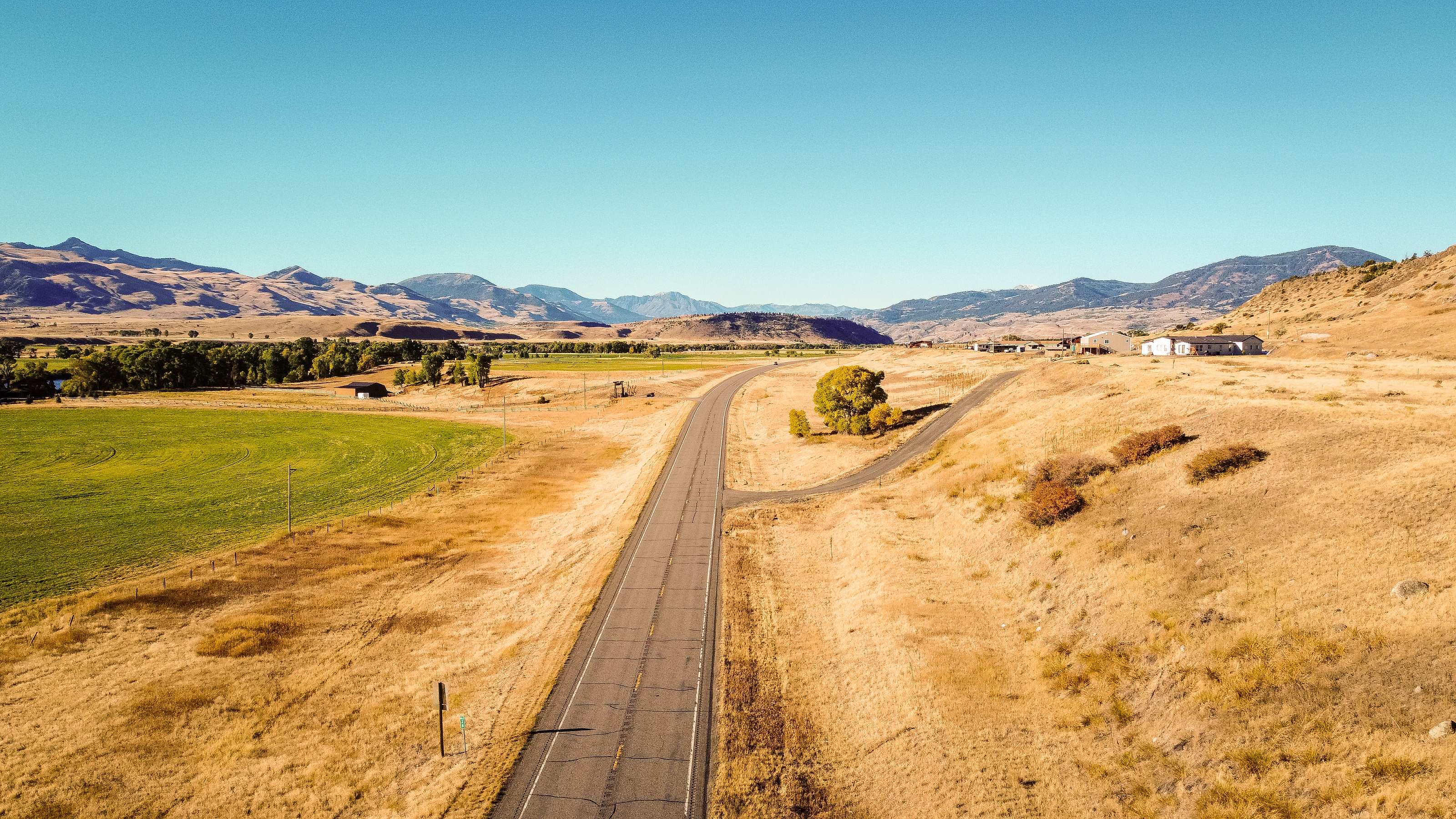 Lonely road seen from above through dry Montana countryside with one house in the background