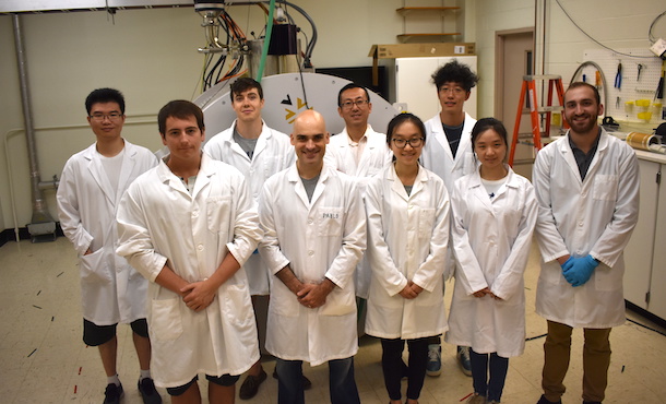 A group of scientists in lab coats posing in front of an MRI machine