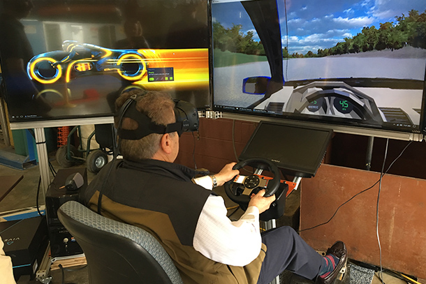 Man sitting in front of large TV screens driving an augmented reality vehicle