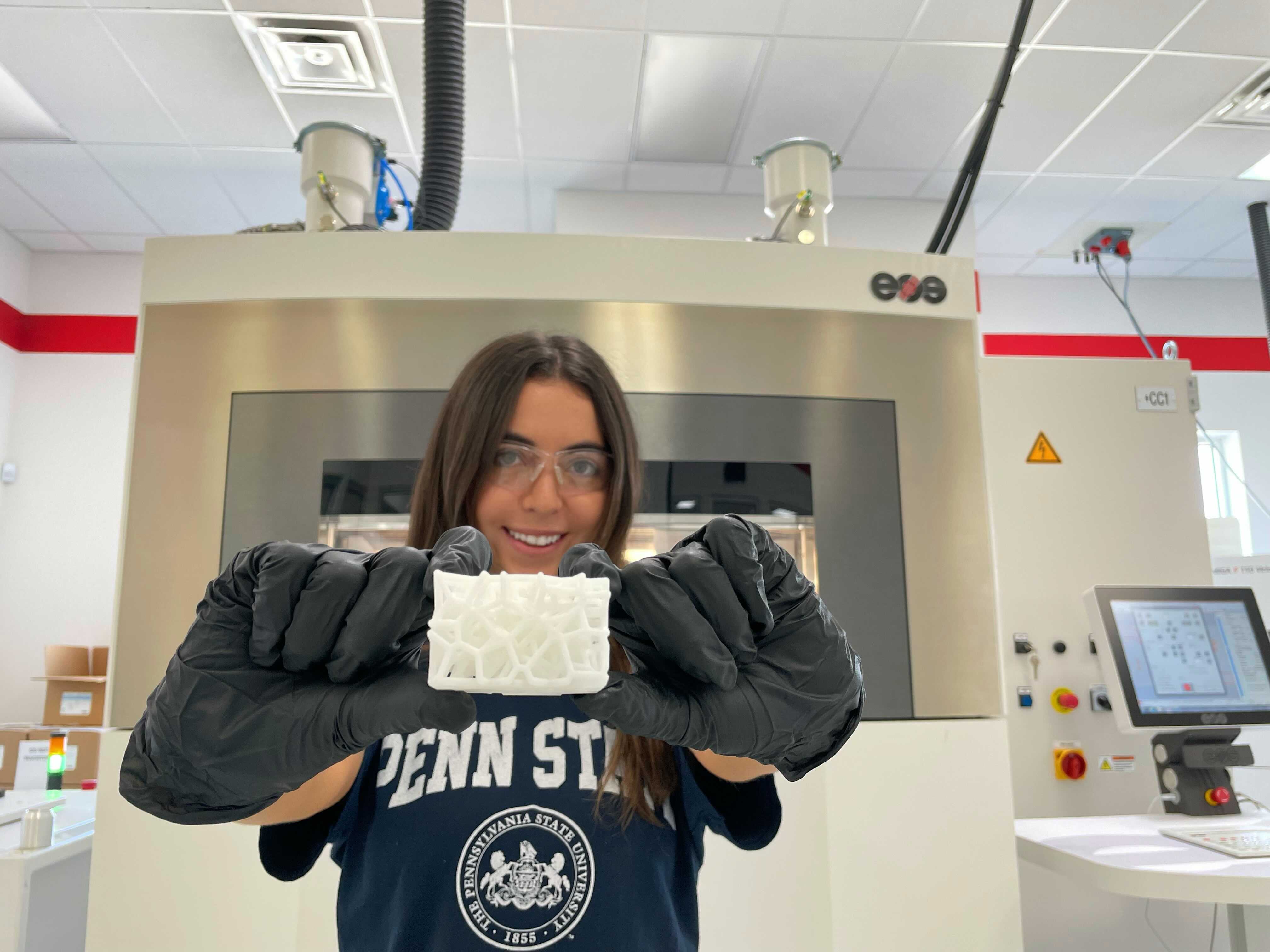 A student in protective lab gear holds up a 3D printed lattice structure.