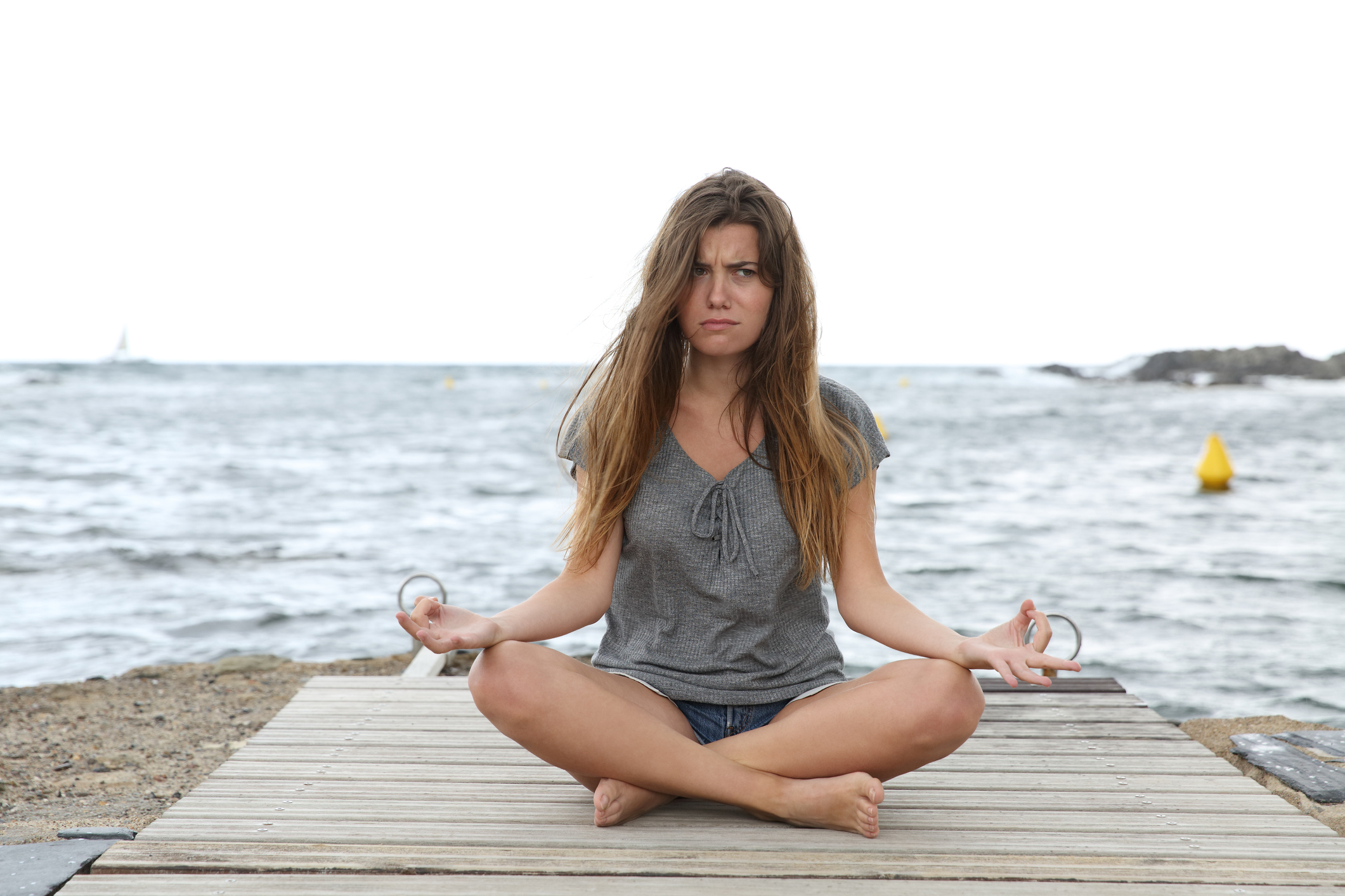 A woman sitting on a beach meditating with a worried expression