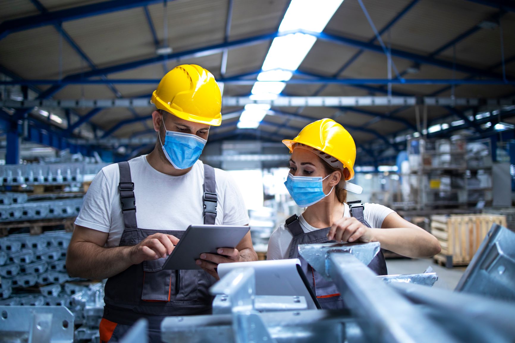 Two masked manufacturing workers in a manufacturing/factory setting