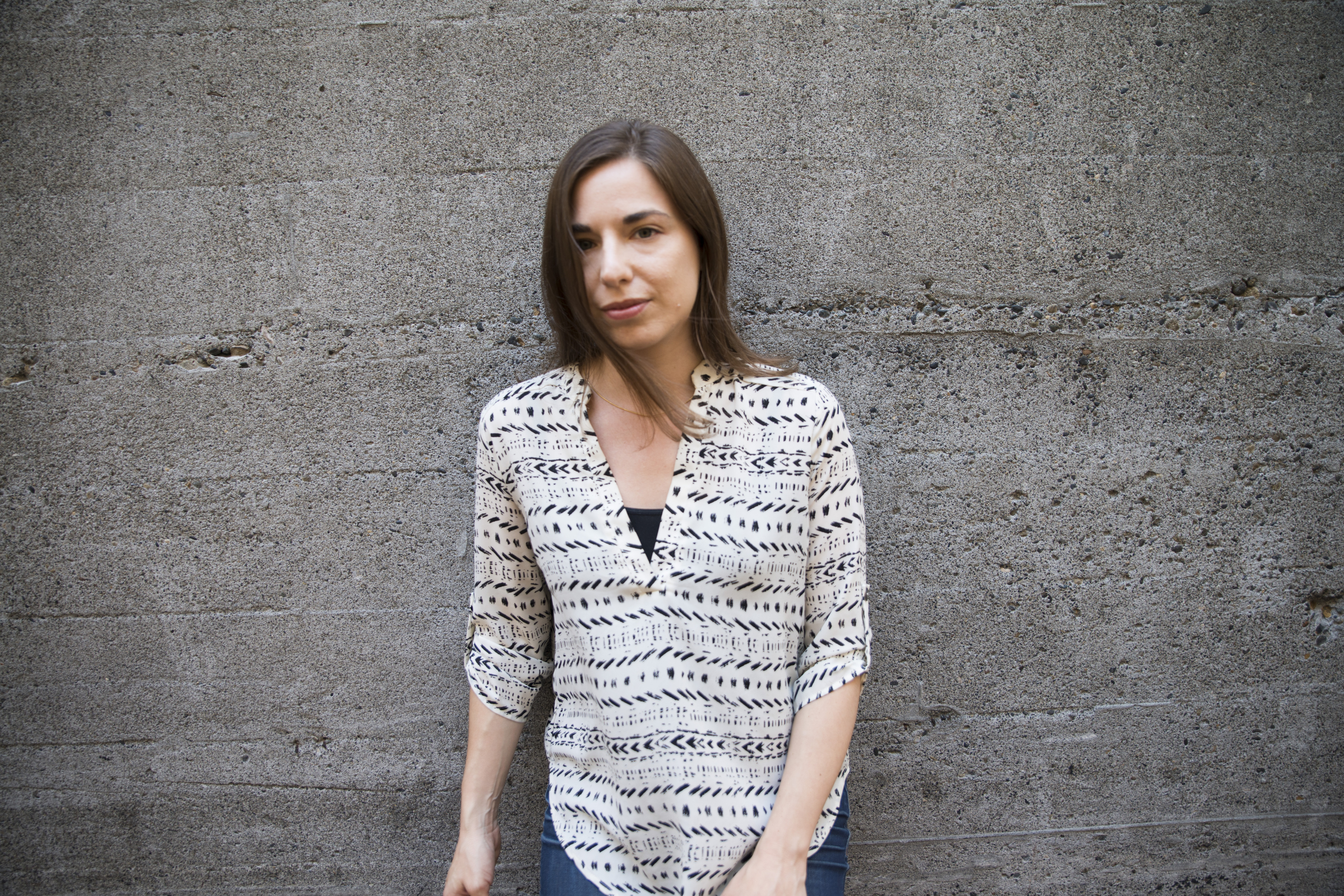 horizontal portrait of Sarah Glidden standing, leaning against concrete wall