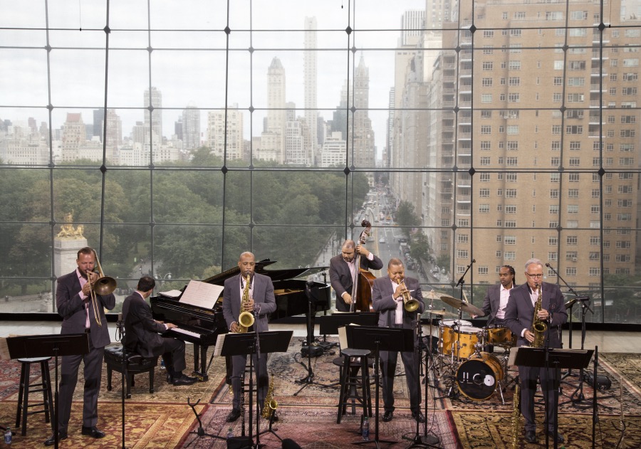 Jazz musicians perform at Lincoln Center in front of window with New York City as backdrop.