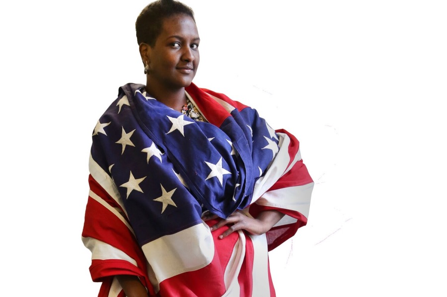 A woman stands with an American flags draped around her shoulders.