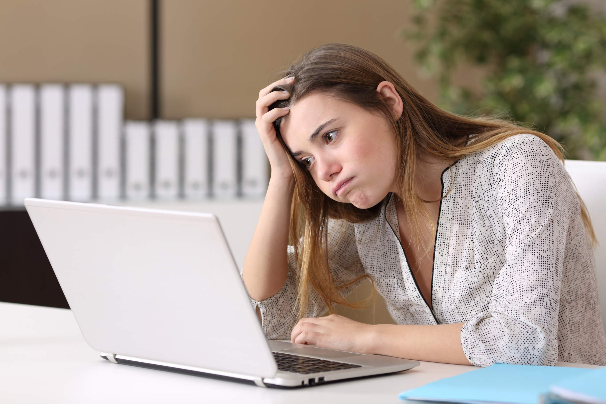 A teen girl sitting in front of a laptop with her head resting on her hand