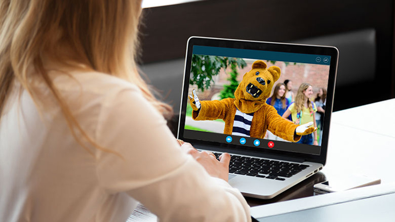 A woman chatting with the Nittany Lion on her laptop