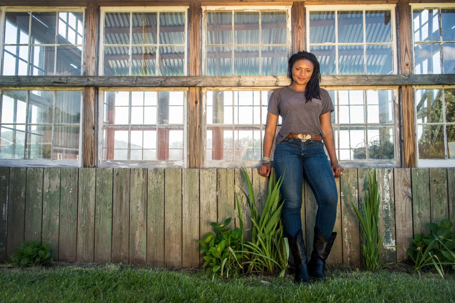 A woman leans against a row of windows and smiles.