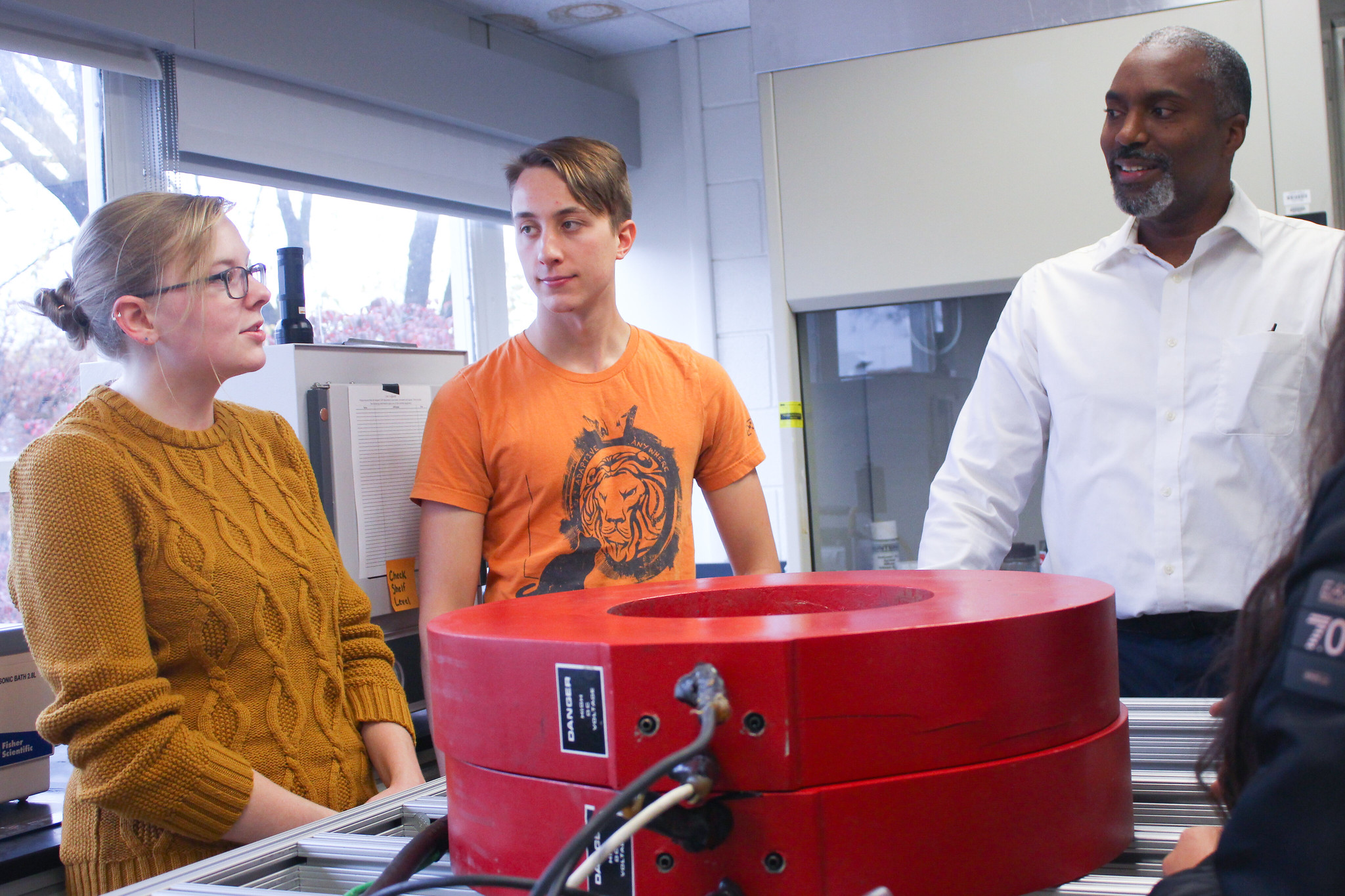 Two graduate students and a professor stand near a magnetic separation device, discussing their research.