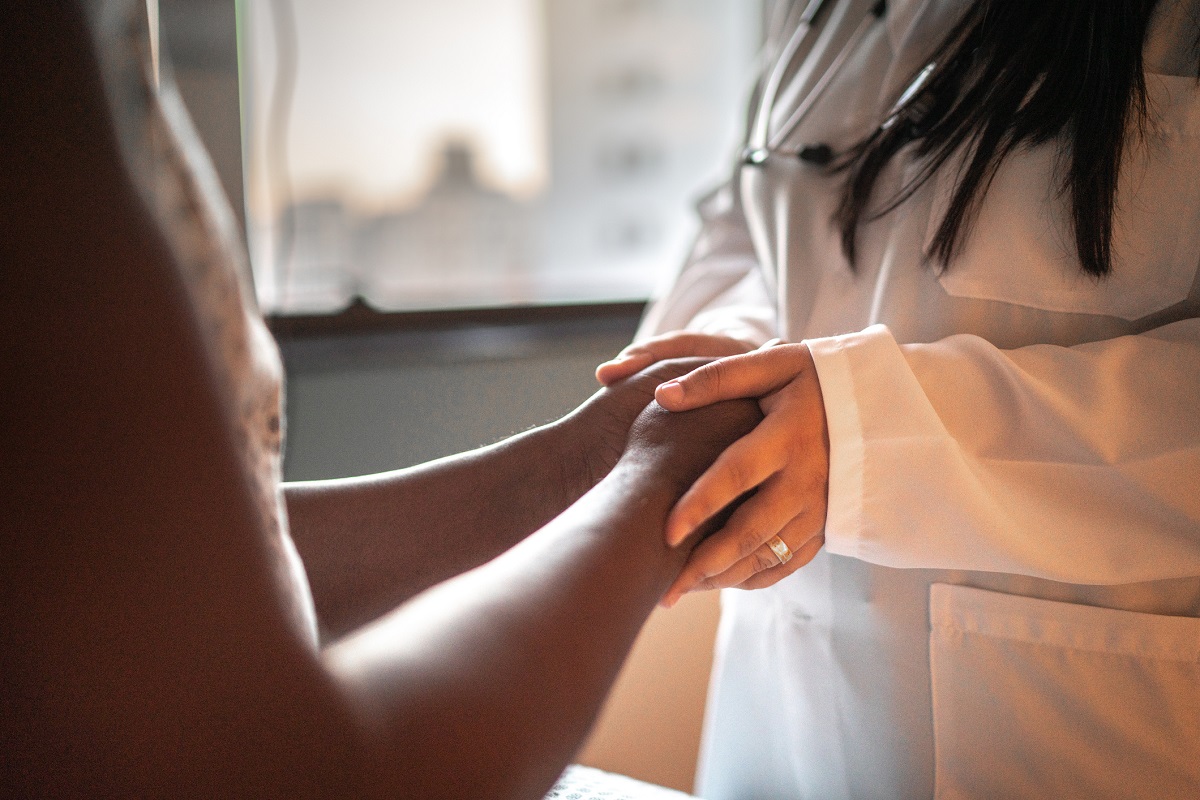 A female doctor holds the hands of her patient in a hospital room.