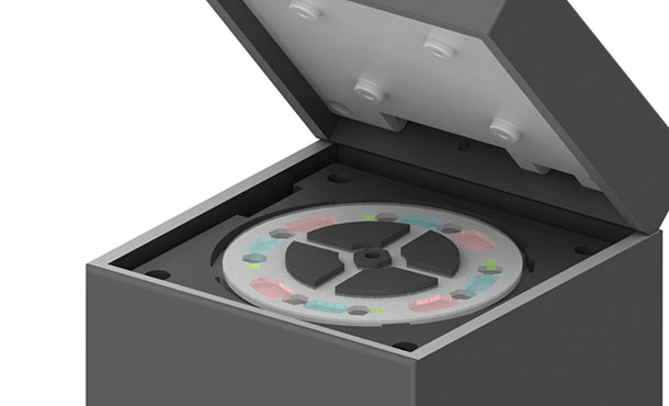 An illustration of a device that resembles a gray box with the lid lifted. On the top of the box under the lifted lid is a disk-like object. 