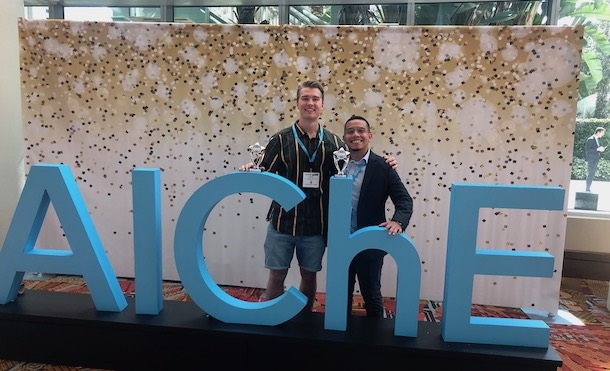 Two young men standing in front of large letters spelling out "AIChE"