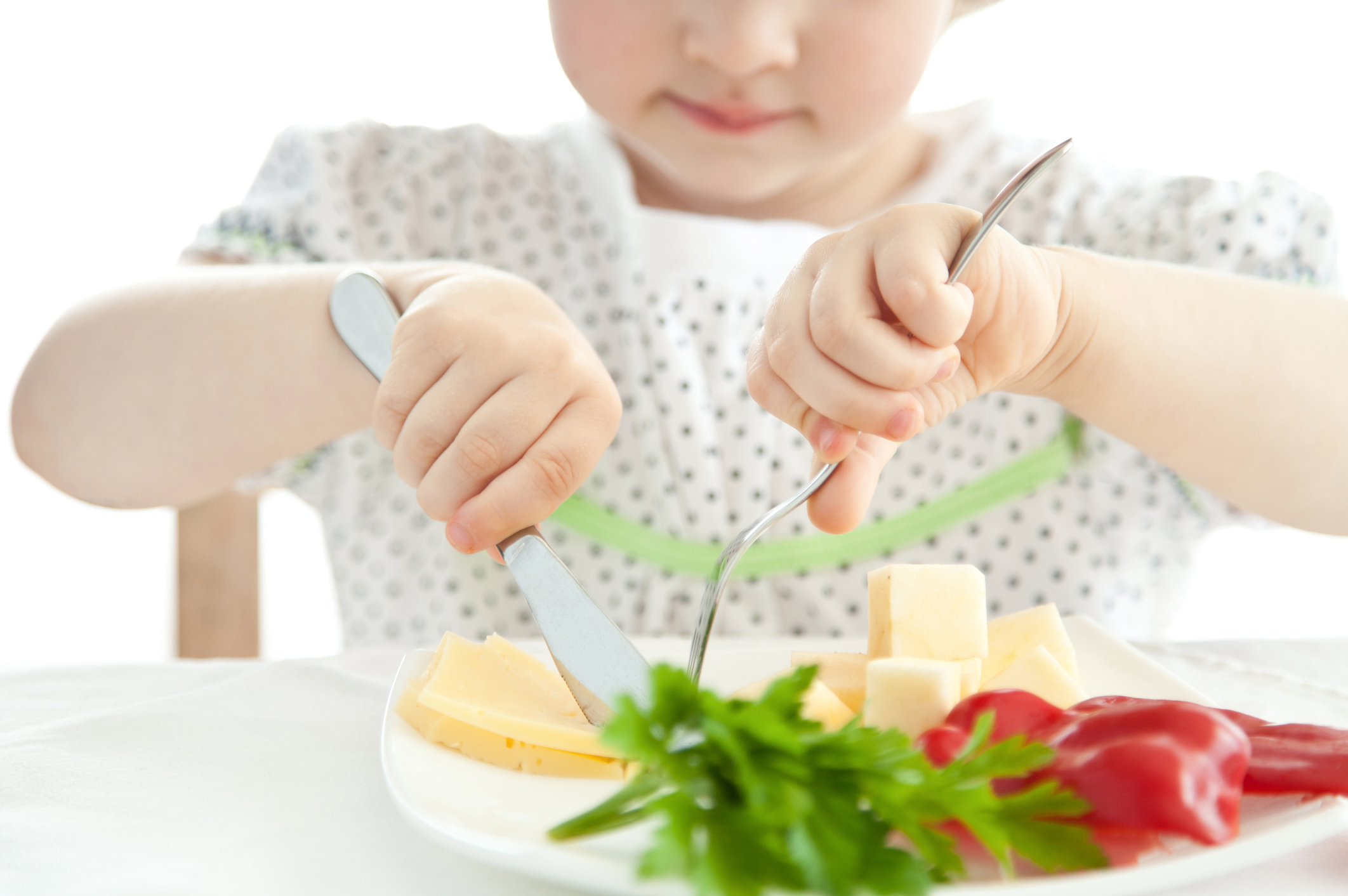 A young child using a knife and fork to eat a plate of vegetables