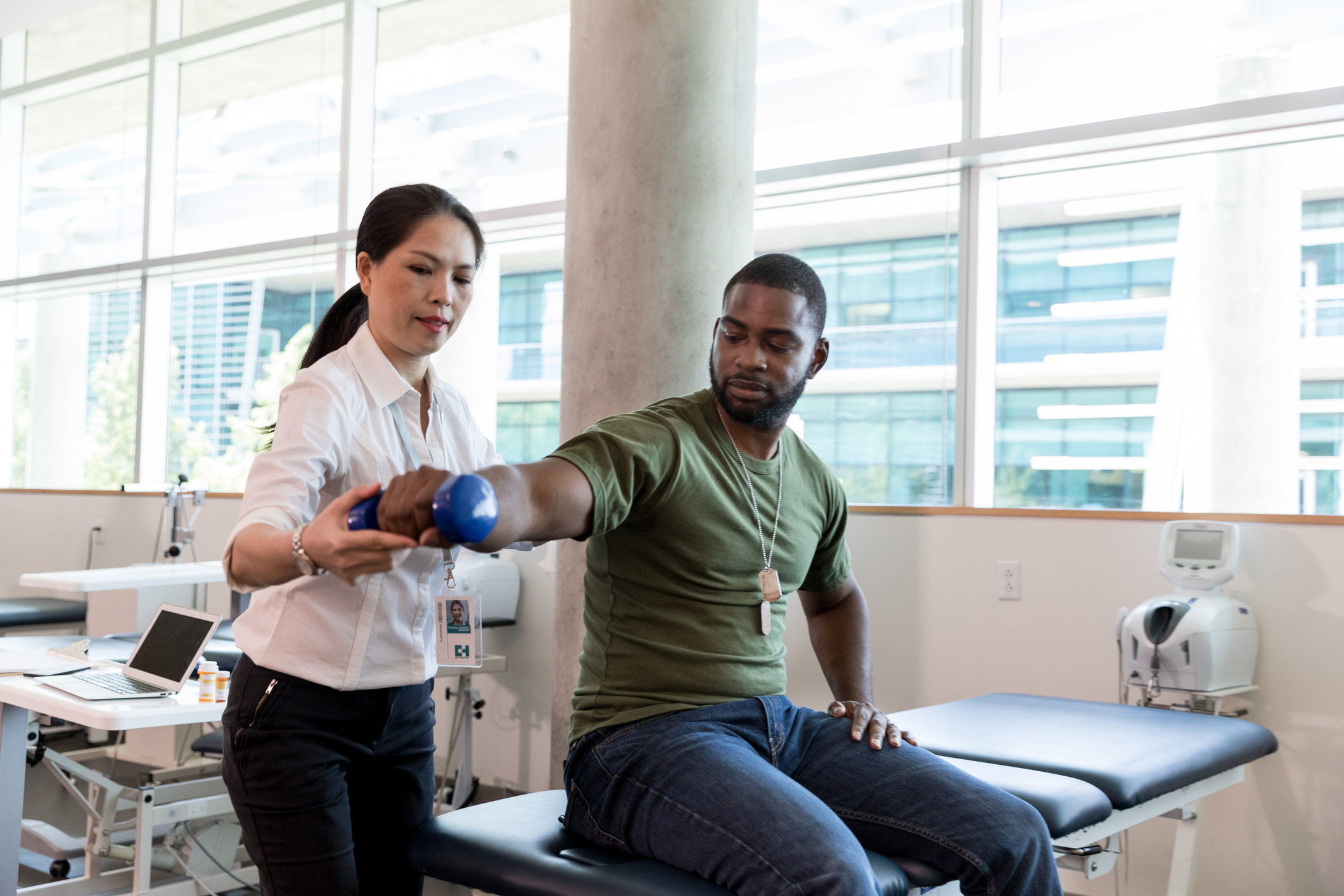 A female doctor helps a male veteran patient with physical therapy on his arm.