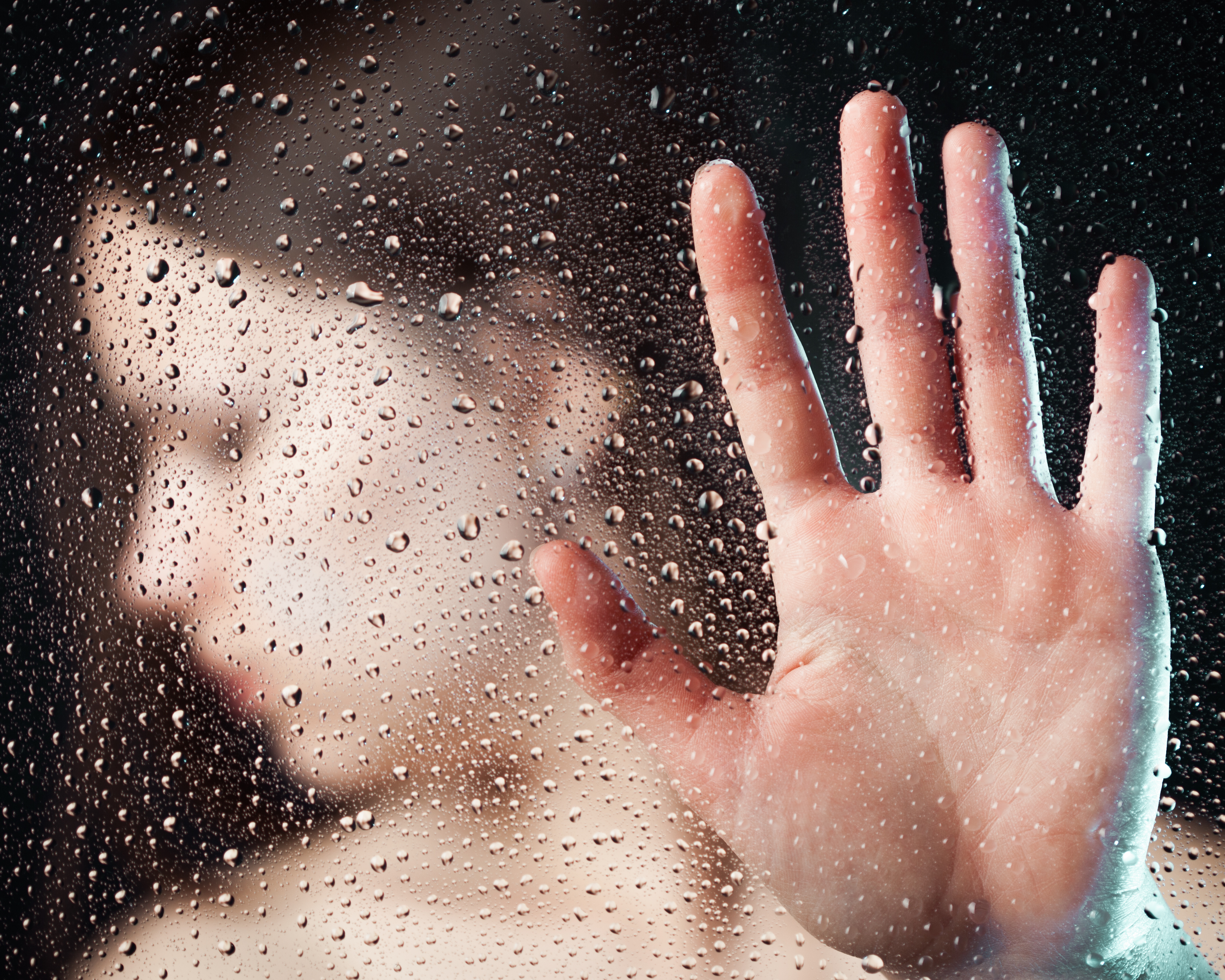 Depressed woman behind glass with her hand up