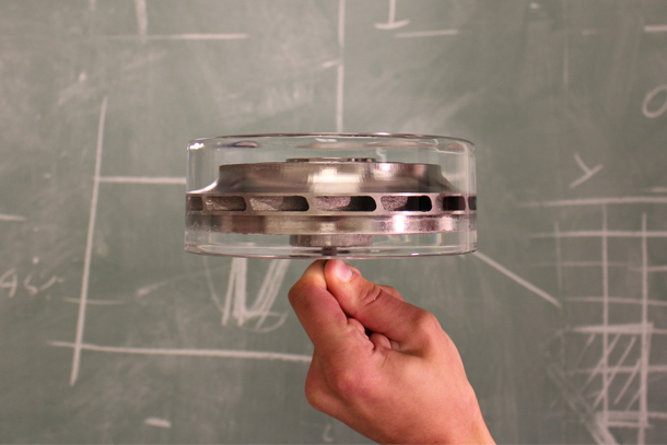 A hand holds a cylindrical metal part almost entirely encased in a cylindrical block of crystal-clear ice.