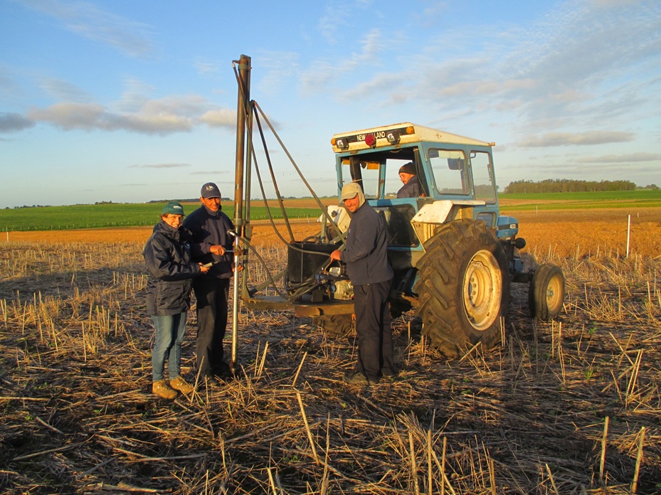 Farmers stand in a field with a tractor. 