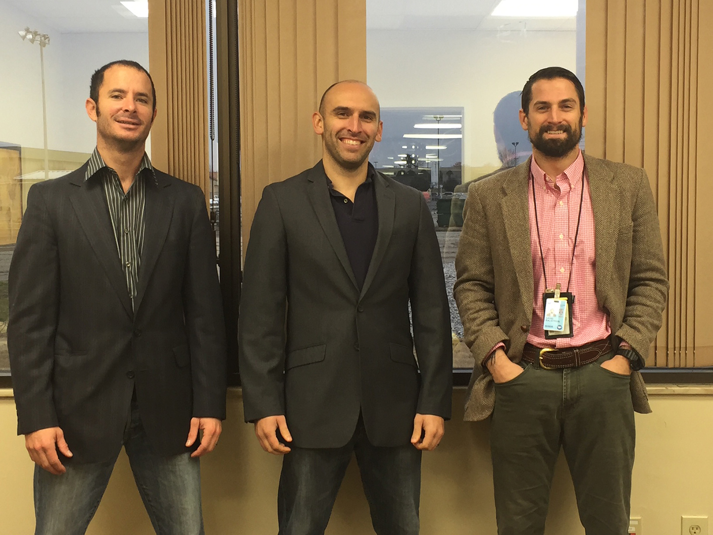 Three men stand together and smile for the camera.