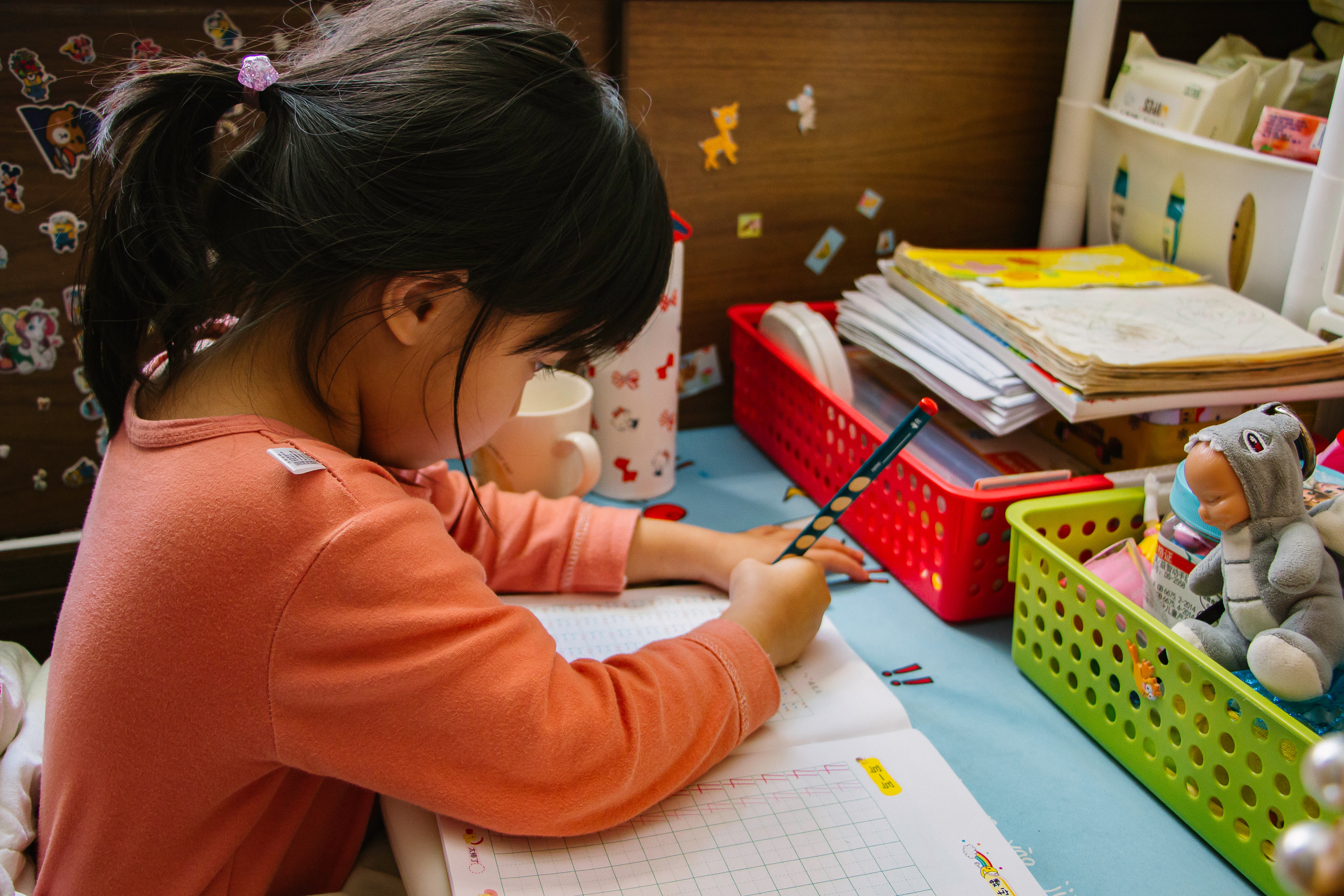 Young girl with black pony tail and orange shirt completing worksheet