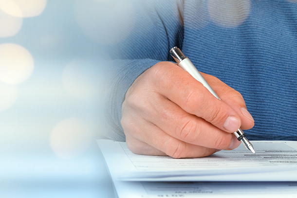 Hand holds a pen and writes on a piece of paper