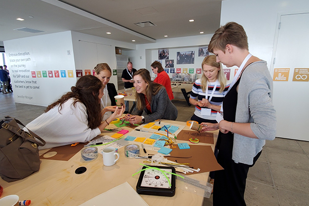 Five people stand around a table covered in Post-its, pipecleaners and cardboard. 