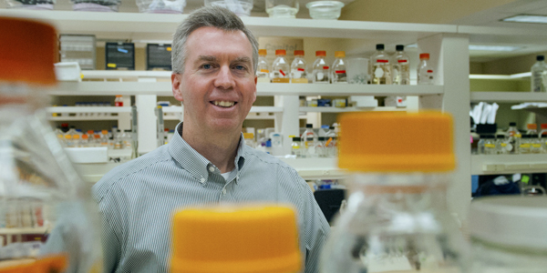 man smiling in lab with clear bottles in the foreground