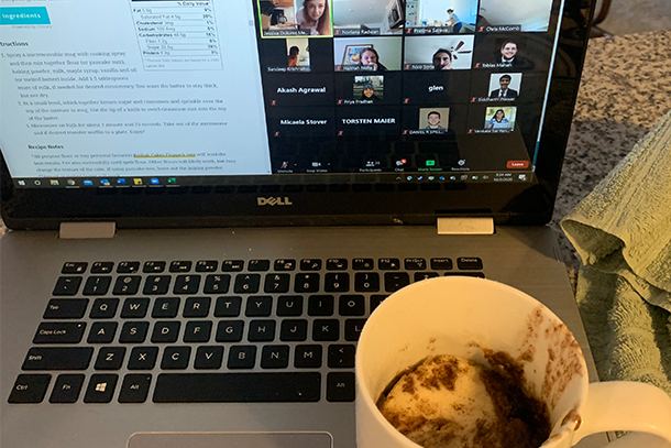 Coffee mug with cake sits near a laptop featuring a Zoom call. 