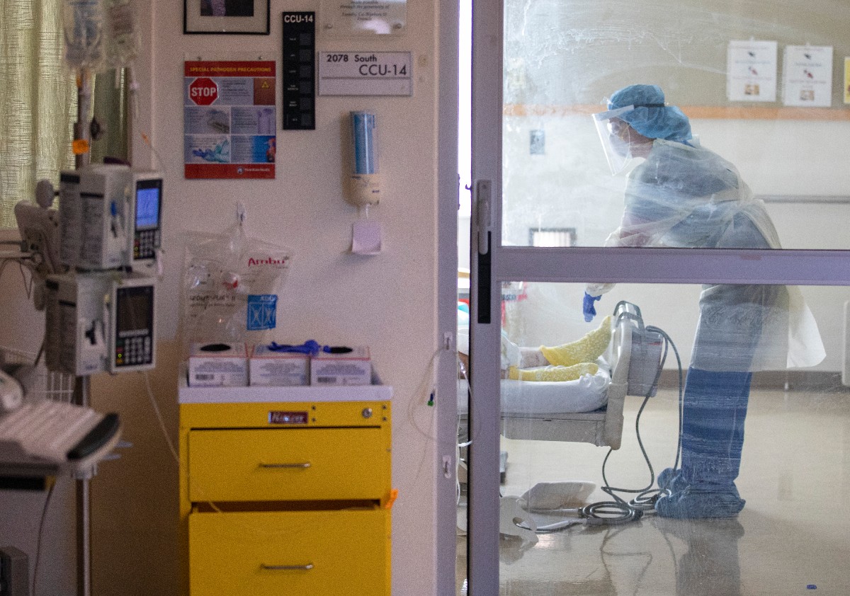 A doctor wearing PPE stands at the foot of a patient's bed in a COVID-19 unit.