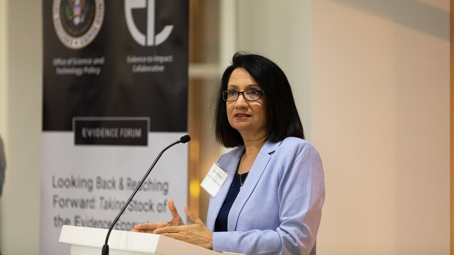 Penn State President Neeli Bendapudi speaks at a podium in front of a banner displaying the White House Office of Science and Technology Policy and Penn State's Evidence-to-Impact Collaborative