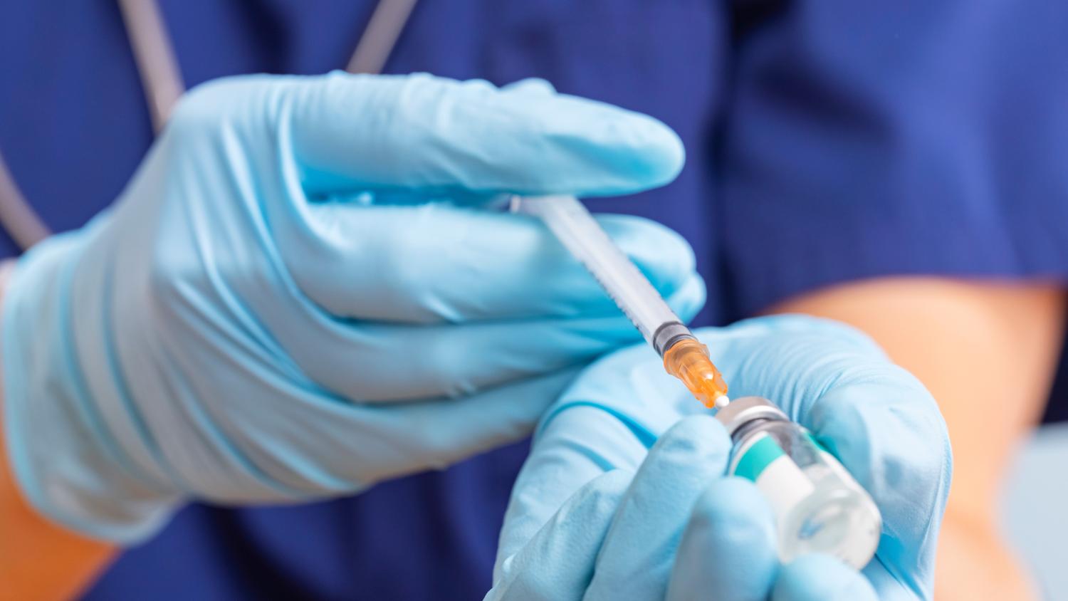 Close-up image of health care professional filling syringe with medicine from a vial