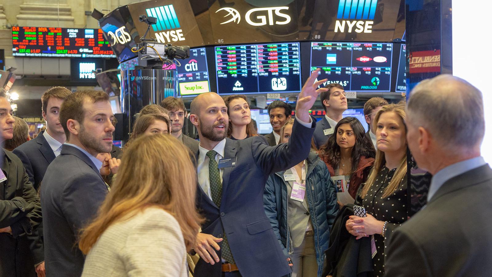 students watch man pointing at NYSE floor
