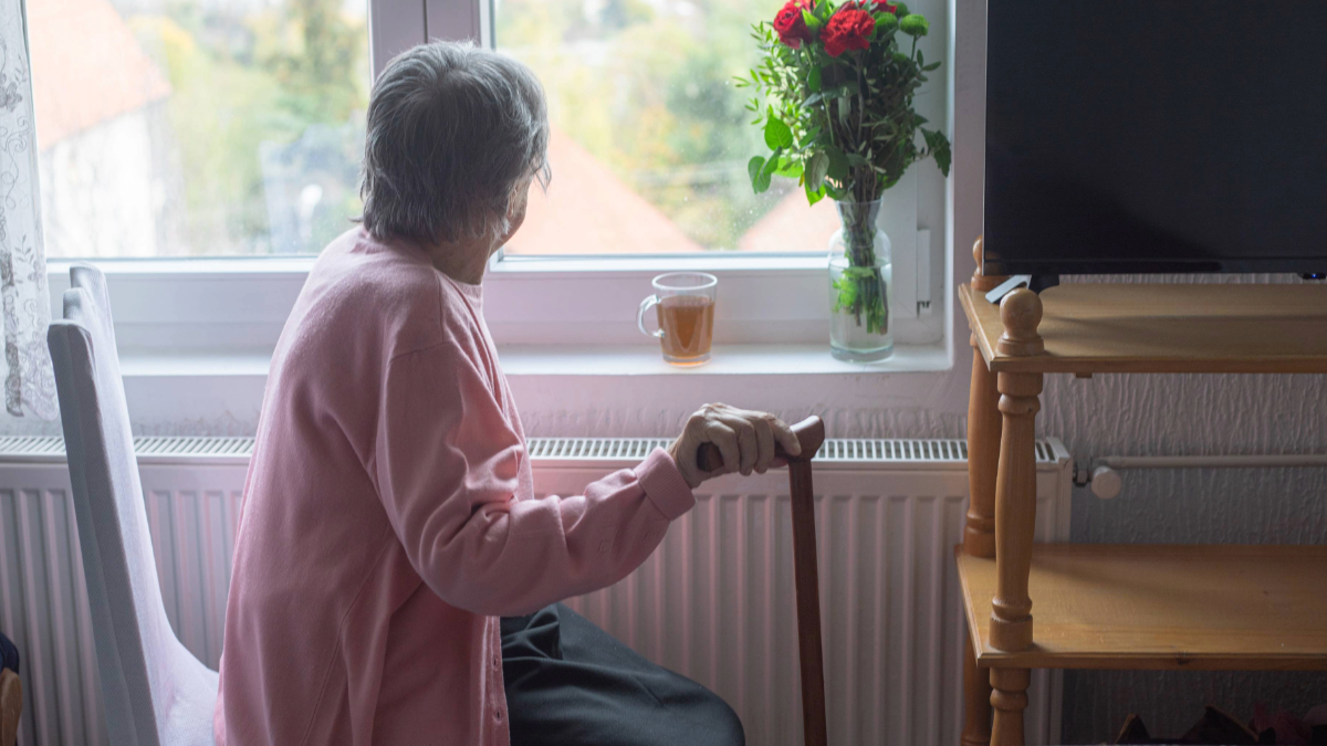 A senior woman holding a cane, looking out a window