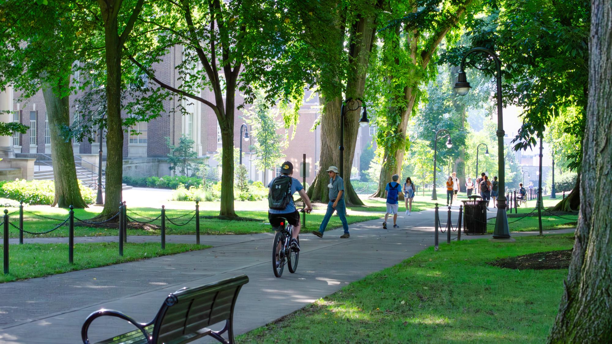 The sidewalk of Henderson building with a person biking and people walking. 