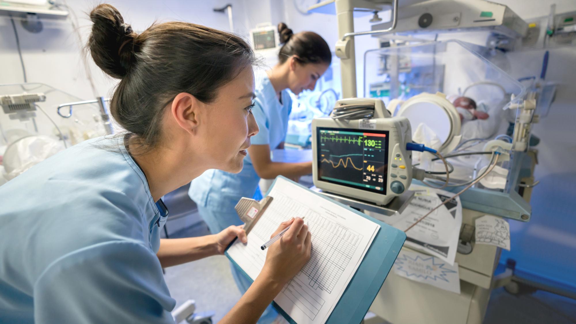 Two nurses monitor a baby in a neonatal intensive care unit