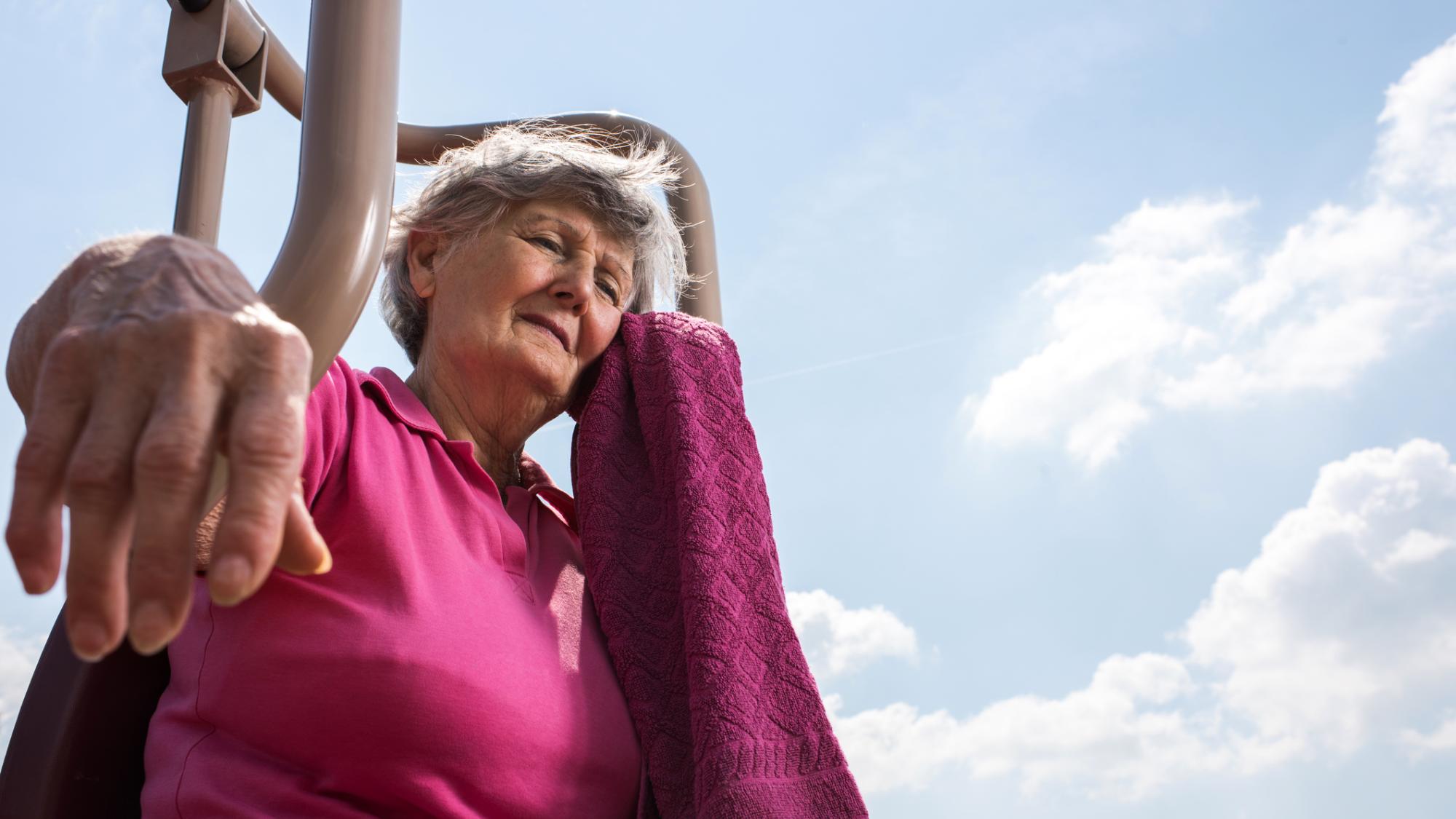 An older woman leans mops her brow in the sunshine
