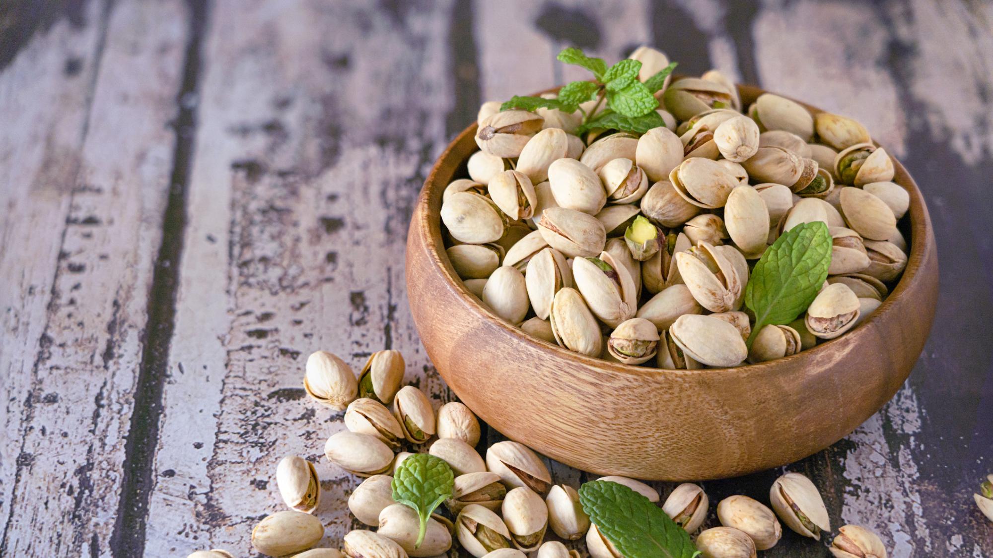 A small wooden bowl overflowing with pistachios and topped with sprigs of mint