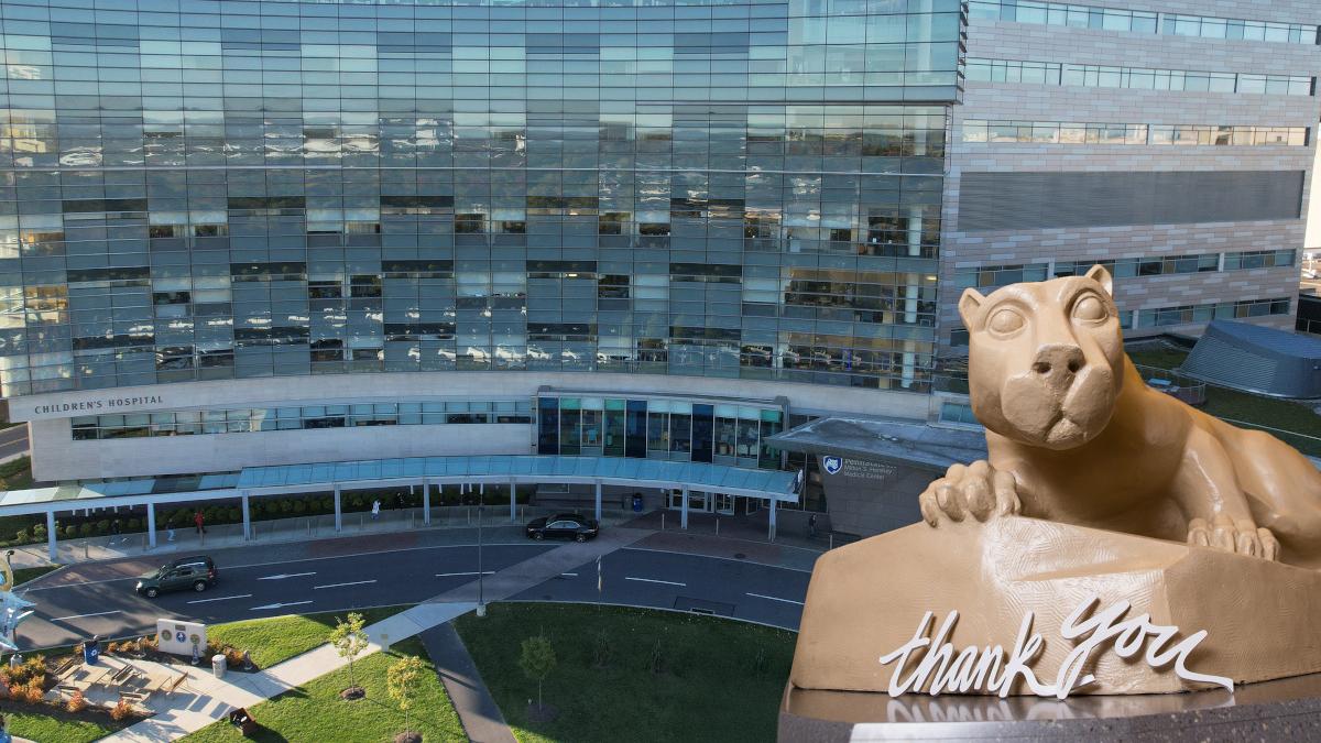 A statue of the Penn State Nittany Lion with the words "thank you" placed in front of it, is superimposed over an exterior image of Penn State Health Children's Hospital.