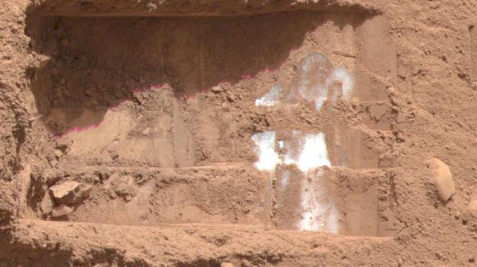 Reddish Martian soil is seen with flecks of Martian ice.