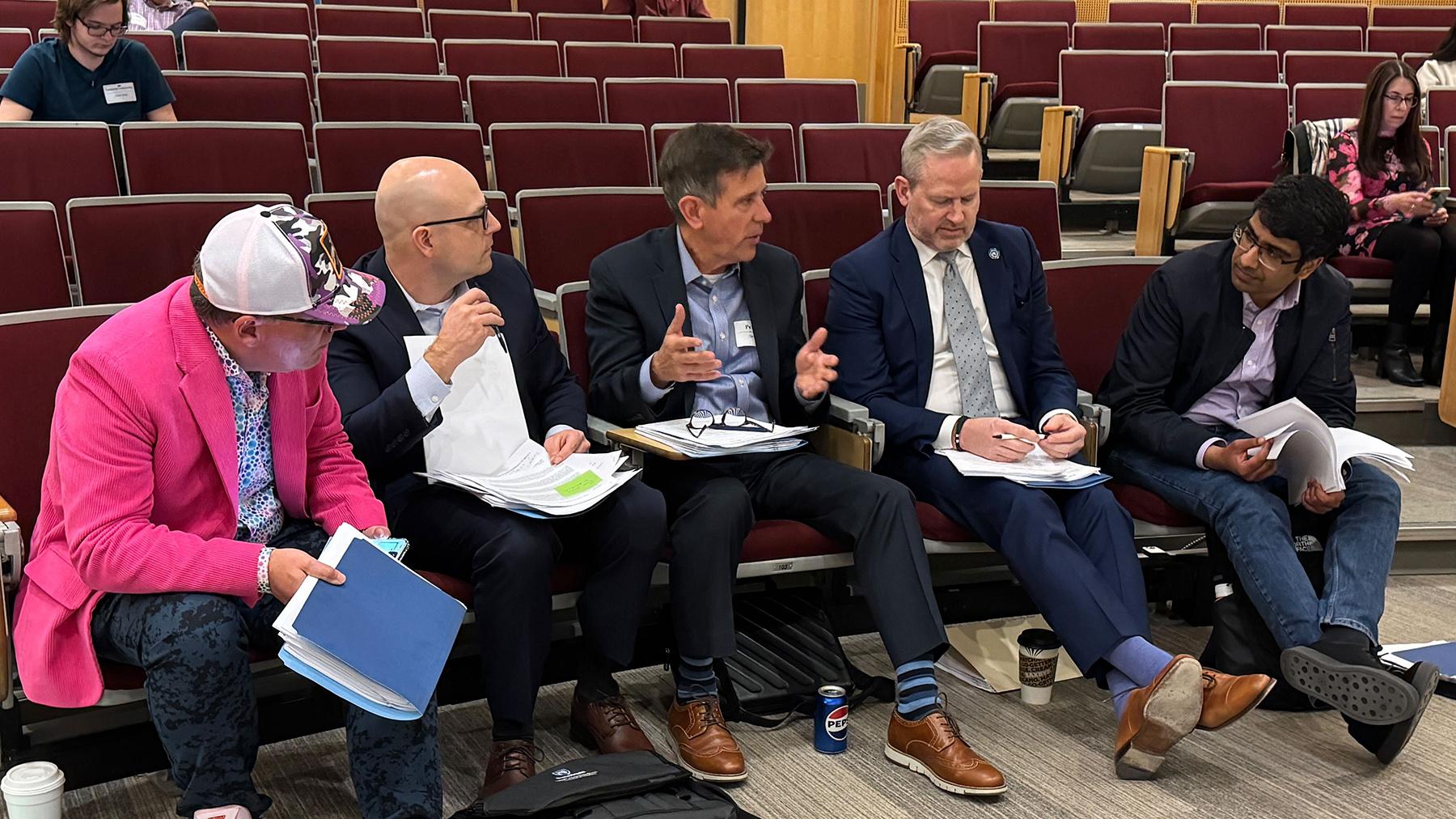 five people serving as case competition judges sit in auditorium seats talking