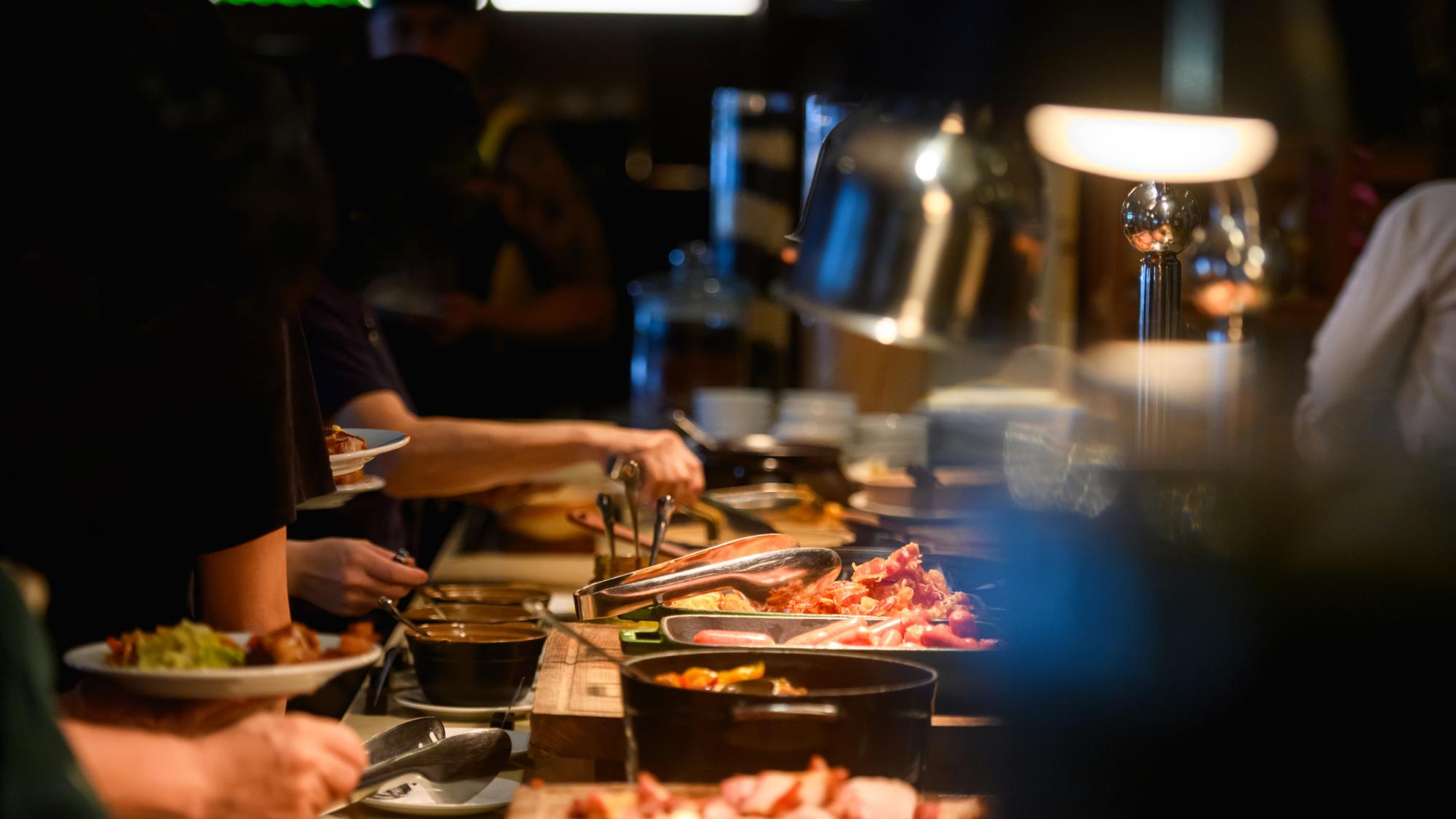 plates held over a long buffet with several types of meat and other foods