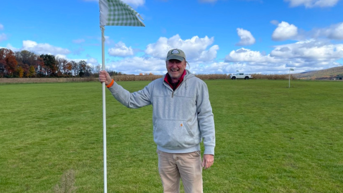 David Huff stands holding a golf flag on a golf course